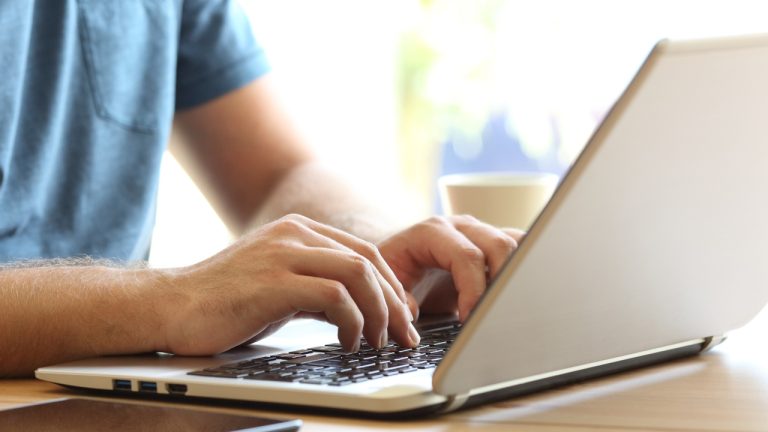 Close up of man hands typing on a laptop keyboard on a desk at home or office